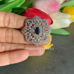 May include: A silver-toned, star-shaped pendant with a rectangular, dark blue center stone. The pendant is surrounded by clear, sparkling accent stones. The text "Penandpendant" is visible at the bottom of the image.