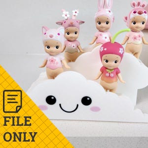 Könnte beinhalten: Eine Sammlung kleiner, dekorativer Figuren in verschiedenen Tier- und Obstkostümen, darunter eine Katze, ein Reh, ein Hase und eine Kirsche. Die Figuren sind hauptsächlich rosa und weiß und stehen auf einem weißen, wolkenförmigen Display.