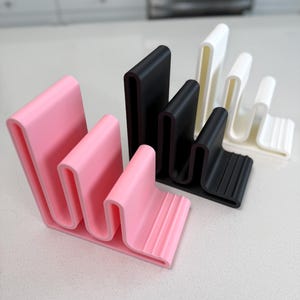 May include: A selection of wavy-shaped kitchen organisers in pink, black, and white. These items are designed to hold kitchen utensils and tools, offering a stylish and functional storage solution for the home.