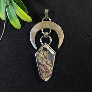 Può includere: Un ciondolo a forma di mezzaluna d'argento con un cristallo di quarzo trasparente che presenta un'inclusione verde e rosa. Il ciondolo è su uno sfondo nero.