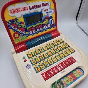 May include: A VTech Little Smart Letter Fun toy laptop. The toy has a yellow top with a train graphic and the words "Letter Fun With Phonics." It features a keyboard with letters and numbers, and a small screen.