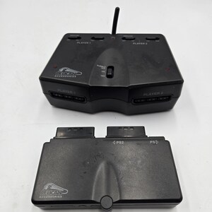 May include: Two black Pelican Accessories PS2 game controllers. The top controller has an antenna and is labeled "PLAYER 1" and "PLAYER 2". The bottom controller is labeled "PS2" and "PS".
