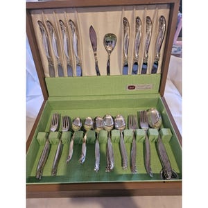 May include: A wooden silverware case with a green felt interior, holding a complete set of silver-colored flatware. The set includes knives, forks, spoons, and serving utensils, all neatly arranged. The case is open, revealing the contents.
