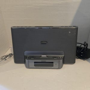 May include: A gray Sony personal audio docking system with a built-in speaker. The docking station has a silver base with function buttons and a slot for a device. A power cord and audio cable are connected to the system.