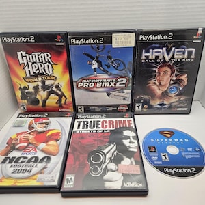 May include: A collection of PlayStation 2 video game cases and a disc. Games include "Guitar Hero World Tour", "Mat Hoffman's Pro BMX 2", "Haven: Call of the King", "NCAA Football 2004", "True Crime: Streets of LA", and "Superman Returns".