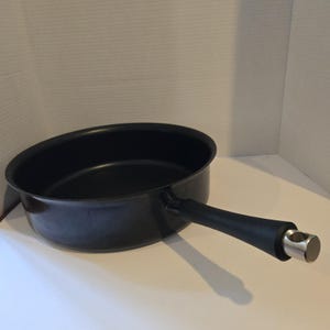 May include: A black saucepan with a long, black handle and a silver-colored metal end. The pan is round with a slightly sloped side. The handle is attached to the side of the pan.