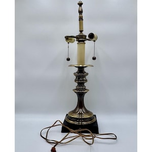 May include: A vintage brass table lamp with a dark brown base. The lamp features a candlestick design with a central light and two side lights. The lamp has a brown cord and a black base. The lamp is approximately 24 inches tall.