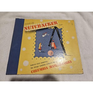 May include: Vintage vinyl record album cover for Tchaikovsky's Nutcracker Suite, featuring a whimsical illustration. The cover has a yellow border with white polka dots, a blue background, and the text "COLUMBIA MASTERWORKS".