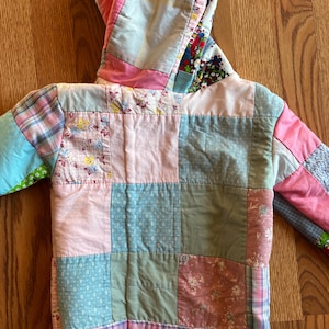 May include: A patchwork jacket with a hood, featuring a variety of pastel-colored fabrics. The jacket is made of squares of pink, blue, green, and floral patterned materials. The hood and sleeves also incorporate different fabric patterns, creating a unique, handcrafted look.