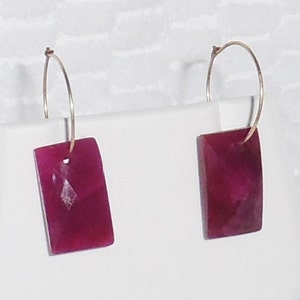 May include: A pair of gold hoop earrings with a rectangular, deep pink stone pendant on each hoop.
