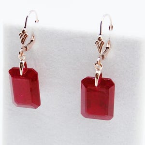 May include: A pair of leverback earrings featuring rectangular, faceted, deep red gemstones. The earrings have gold-colored metal accents and a classic, elegant design. The gemstones are approximately 0.75 inches in length.