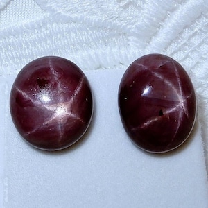 以下が含まれることがあります： 6 本の尖った星形の模様が入った、赤色の楕円形のスターサファイアカボションが 2 つ。石は磨かれた滑らかな仕上げでセットされています。