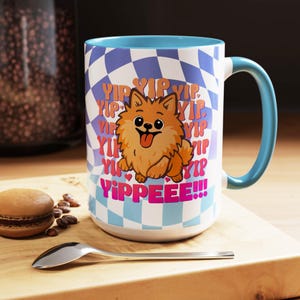 Puede incluir: Una taza grande de cerámica blanca con interior y asa azules. La taza presenta una ilustración de perro Pomerania de dibujos animados con las palabras "YIP YIP YIP" y "YIPPEEE!!!" en rosa y amarillo. El fondo tiene un patrón de cuadros azules y blancos.