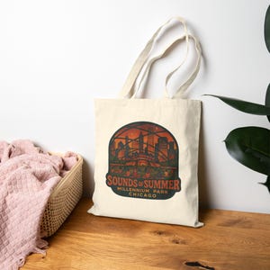 Puede incluir: Bolso tote de color crema con un gráfico del horizonte de Chicago al atardecer. El diseño incluye el texto "Sounds of Summer" y "Millennium Park Chicago" en un estilo vintage. El bolso tiene dos asas.