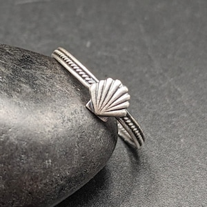 May include: A silver ring with a seashell design. The ring is twisted and has a rope-like texture.