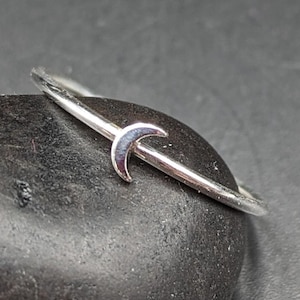 May include: A silver ring with a crescent moon design. The ring is thin and delicate, and the moon is small and simple.
