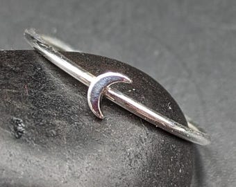 May include: A silver ring with a crescent moon design. The ring is thin and delicate, and the moon is small and simple.