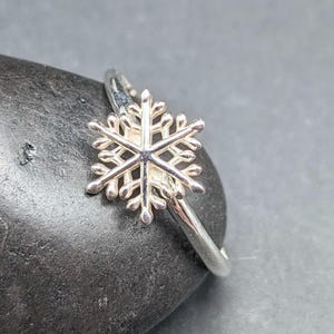 May include: A silver ring with a delicate snowflake design. The ring is simple and elegant, perfect for everyday wear.