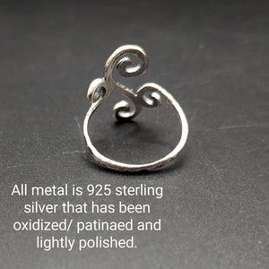May include: Sterling silver ring with an oxidized finish. The ring features a swirling design with a textured band. The text in the image reads: "All metal is 925 sterling silver that has been oxidized/ patinaed and lightly polished."