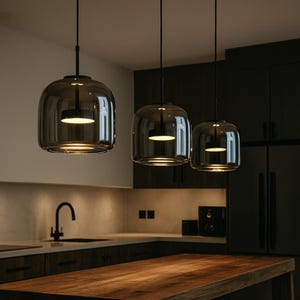 Peut inclure: Trois lampes suspendues modernes avec des abat-jours en verre fumé sont suspendues au-dessus d'un plan de travail en bois. Chaque lampe a une base circulaire éclairée. La cuisine comprend des meubles sombres et un robinet en acier inoxydable.