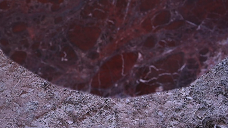 Peut inclure: Gros plan sur une surface de marbre rouge fonc&eacute; avec des veines blanches. Le marbre poli contraste avec une surface de pierre grise rugueuse. L'image montre une section du marbre.