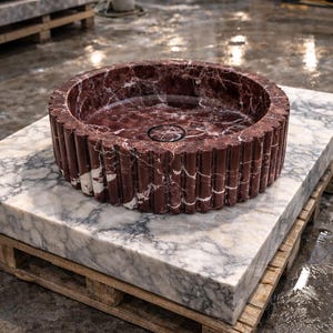 Peut inclure: Un &eacute;vier rond en marbre rouge vein&eacute; de blanc, pos&eacute; sur une dalle de marbre sur une palette en bois. L'&eacute;vier a un ext&eacute;rieur cannel&eacute; et un drain circulaire. Le design est moderne et luxueux, adapt&eacute; &agrave; une salle de bain.