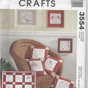 May include: A McCall's Crafts sewing pattern envelope 3554 featuring illustrations of embroidered pillows and a quilt. The designs include red and white fabric squares with stitched motifs of houses, flowers, hearts, and angels with text.