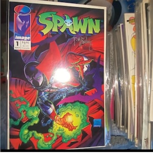 以下が含まれることがあります： 赤いマントと鎖を身につけた暗い姿が特徴の、Spawnコミックブック、1号。タイトル「Spawn」は緑と青。表紙にはサインとImage Comicsのロゴが入っています。