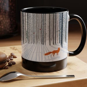 Könnte beinhalten: Schwarz-weiße Keramik-Tasse mit einer Winterwaldszene und einem orangefarbenen Fuchs. Die Tasse hat einen schwarzen Innenraum und Henkel. Die Tasse steht auf einer Holzoberfläche mit einem Löffel, einem Macaron und Kaffeebohnen.