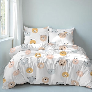 Może przedstawiać: Biały zestaw pościeli z powtarzającym się wzorem twarzy zwierząt z kreskówek w różnych kolorach. Zestaw zawiera poszwę na kołdrę i dwie poszewki na poduszki. Twarze zwierząt obejmują niedźwiedzie, psy, koty i króliki.