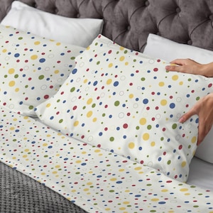 May include: White bedding set with a colorful polka dot pattern. The pattern includes red, yellow, blue, and green dots of varying sizes. The set includes a fitted sheet and pillowcases.