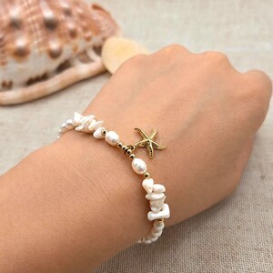 Op de afbeelding: Een armband met witte onregelmatige schelpfragmenten en gladde witte parels, afgewisseld met kleine goudkleurige kraaltjes. Een goudkleurige zeester-bedel hangt aan het midden van de armband, die bestaat uit een mix van organische texturen en accenten.