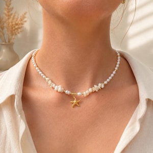 Op de afbeelding: Een ketting bestaande uit een streng kleine witte parels en onregelmatige witte schelpkralen. Een goudkleurige zeesterhanger hangt in het midden van de ketting. Het sieraad wordt om de hals gedragen en toont het contrast tussen de witte kralen en de metalen gouden zeesterhanger.