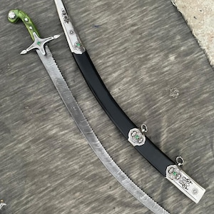 May include: A curved sword with a serrated Damascus steel blade, a green handle, and a silver crossguard featuring a green stone. The accompanying black scabbard has silver metal fittings decorated with intricate engravings and green stone accents.