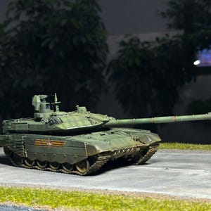 Może przedstawiać: Szczegółowy model zielonego czołgu wojskowego z długą lufą, ustawiony na szarej powierzchni z trawiastą krawędzią. Czołg posiada skomplikowane detale, w tym wieżę i gąsienice oraz czerwony emblemat gwiazdy.