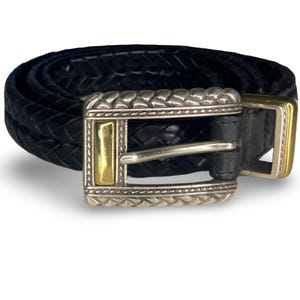 Op de afbeelding: Zwarte gevlochten leren riem met een zilveren en gouden gesp. De gesp heeft een rechthoekige vorm met een zilveren rand en gouden accenten. De riem is opgerold en toont zijn geweven textuur.