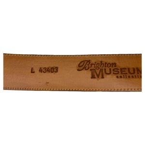 Op de afbeelding: Close-up van de binnenkant van een lichtbruine leren riem. De riem is gestempeld met de woorden "Brighton MUSEUM collection". De maat is gemarkeerd als "L 43403".