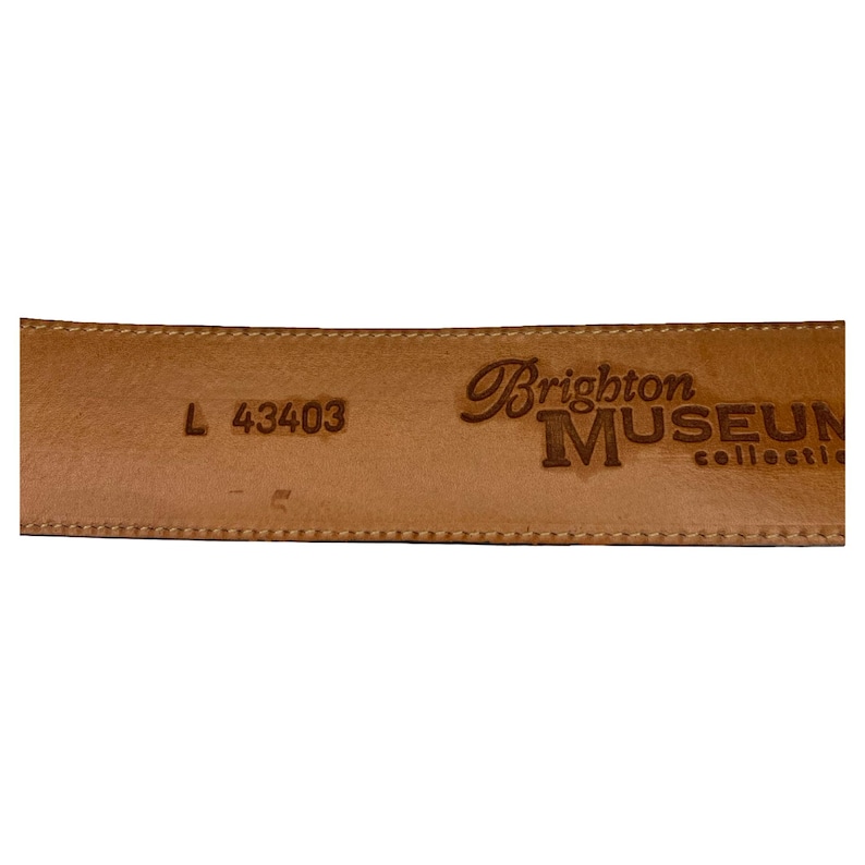 Op de afbeelding: Close-up van de binnenkant van een lichtbruine leren riem. De riem is gestempeld met de woorden "Brighton MUSEUM collection". De maat is gemarkeerd als "L 43403".