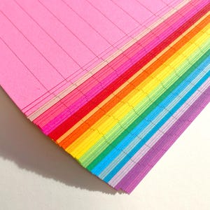 May include: A stack of colorful lined paper in rainbow order, starting with pink and ending with purple.
