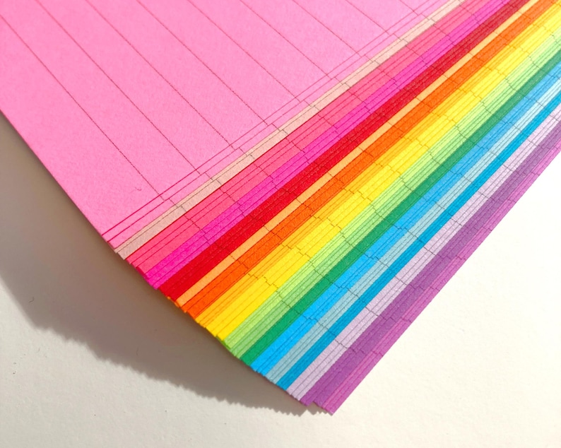 May include: A stack of colorful lined paper in rainbow order, starting with pink and ending with purple.