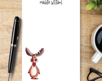 May include: A white rectangular notepad featuring the printed name Maddie Williams at the top and a cartoon illustration of a brown moose with a light tan belly and blue eyes positioned in the lower left corner of the paper sheet.