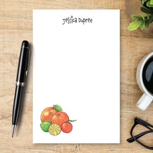 May include: A white rectangular notepad featuring the name Jessica Dupree printed in black at the top center and a colorful watercolor illustration of various citrus fruits, including oranges, a lime, and a lemon slice, at the bottom left corner.