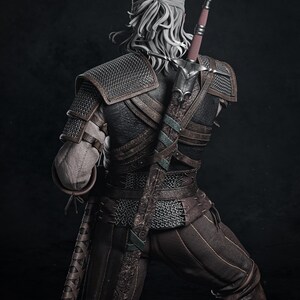 May include: A detailed figurine of a warrior with long white hair tied back, wearing dark brown leather armor with chainmail accents. A long sword in an ornate, dark brown scabbard is strapped to the back, extending above the shoulder.