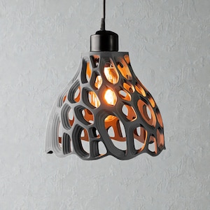 May include: A gray, open-weave pendant light fixture with a black top and a visible lightbulb. The shade has a unique, organic design with numerous oval-shaped openings, allowing the warm light to shine through. The fixture hangs from a black cord.