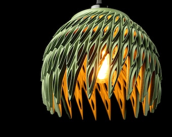 Może przedstawiać: Zielona lampa wisząca o unikalnym, warstwowym designie. Lampa ma szereg podłużnych, przypominających liście wycięć, które pozwalają na przenikanie ciepłego światła z żarówki. Oprawa zwisa z cienkiego drutu na czarnym tle.