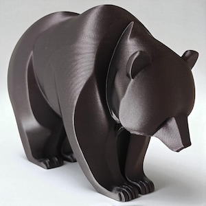 Könnte beinhalten: Dunkelbraune Bärenskulptur mit einem stilisierten, geometrischen Design. Der Bär ist in einer stehenden Position dargestellt, mit leicht gesenktem Kopf. Die Skulptur hat eine glatte, matte Oberfläche.