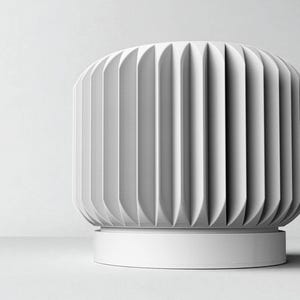 May include: A white, cylindrical decorative object with a ribbed, vertical design. The object has a rounded top and sits on a circular base. The overall aesthetic is minimalist and modern, with a focus on texture and form.