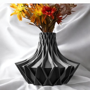 May include: A modern, geometric black vase with a diamond pattern, holding a bouquet of colorful flowers. The vase has a wide base and a narrow neck, and the flowers include yellow, orange, and red blooms. The vase is made of a dark material.