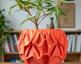May include: A bright orange, geometrically patterned plant pot containing a small green plant. The pot features a unique, textured design and rests on a matching base. The plant has long, slender green leaves and brown stems. The pot is approximately 20 cm in diameter.