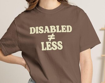Può includere: Una t-shirt marrone a maniche corte con la scritta color crema "DISABLED ≠ LESS" stampata in un carattere grassetto e arrotondato sul petto. Il capo presenta un girocollo e una vestibilità standard con un design grafico ben visibile.